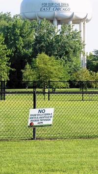 The water tower overlooking an unused ballfield at Carrie Gosch Elementary School says "protecting our children," but a sign from the EPA warns in Spanish that people shouldn't play in the dirt or mulch. (Joe Puchek / Post-Tribune)