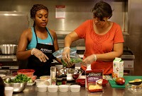 Shannon Smith, left, of NJOY Eats and Preps, teaches a free meal prep class with help from class member Michelle Bibbs, right, last month at ArtHouse: A Social Kitchen in Gary. The culinary business incubator will start hosting weekly workshops from August until October. Staff photo by Jonathan Miano