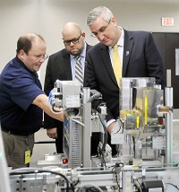 John Wardwell, left, SMC national training manager, explains to Indiana Gov. Eric Holcomb, right, the operation of the HAS-200 Highly Automated System at Purdue Polytechnic for engineering students to learn on, as Cory Sharp, center, director of Purdue Polytechnic, gives the governor a tour of the facility Monday. Staff photo by John P. Cleary