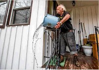 Robert Forler tosses a bucket out water off his front porch as he tries to clear standing water from his home on Emerson Avenue in South Bend Wednesday. Staff photo by Robert Franklin