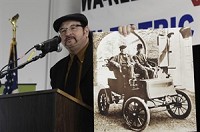 Electric Motors Corp. chief executive officer Wil Cashen holds a photo featuring an electric car from the turn of the last century Thursday as he announces his plans to locate a hybrid vehicle manufacturing facility in the Wakarusa-Nappanee area during a press conference in Wakarusa. Truth photo by Jennifer Shephard
