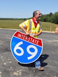 David Goffinet carries an Interstate 69 shield while walking along the southbound lanes as representatives for INDOT offer a tour and give updates to the media about the Interstate 69 project Wednesday. The stretch of Interstate 69 from Evansville to Crane could be completed and open to traffic as early as mid-November. Staff photo by Jason Clark