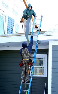 Craig Hill, top, of Hill Construction Co., takes siding from Jeff Ford on Friday while working on a house&nbsp; in the new Triangle subdivision. Staff photo by Greg Swiercz