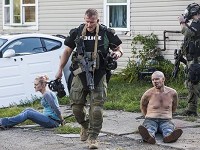 A local police officer walks past handcuffed suspects at the scene of an August 2015 meth raid. Staff file photo byJo rdan Kartholl