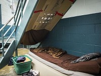 An inmate positioned on a cot in a cell block due to overcrowding uses cardboard to block light in the common area at the Delaware County Jail Wednesday.&nbsp;&nbsp;Staff photo by Jordan Kartholl