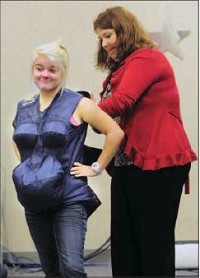 A weighty matter: Greenfield-Central sophomore Raven Gilleland gets assistance from teacher Michelle Overman as she dons an Empathy Belly. The bodysuit is meant to mimic pregnancy. Staff photo by Tom Russo