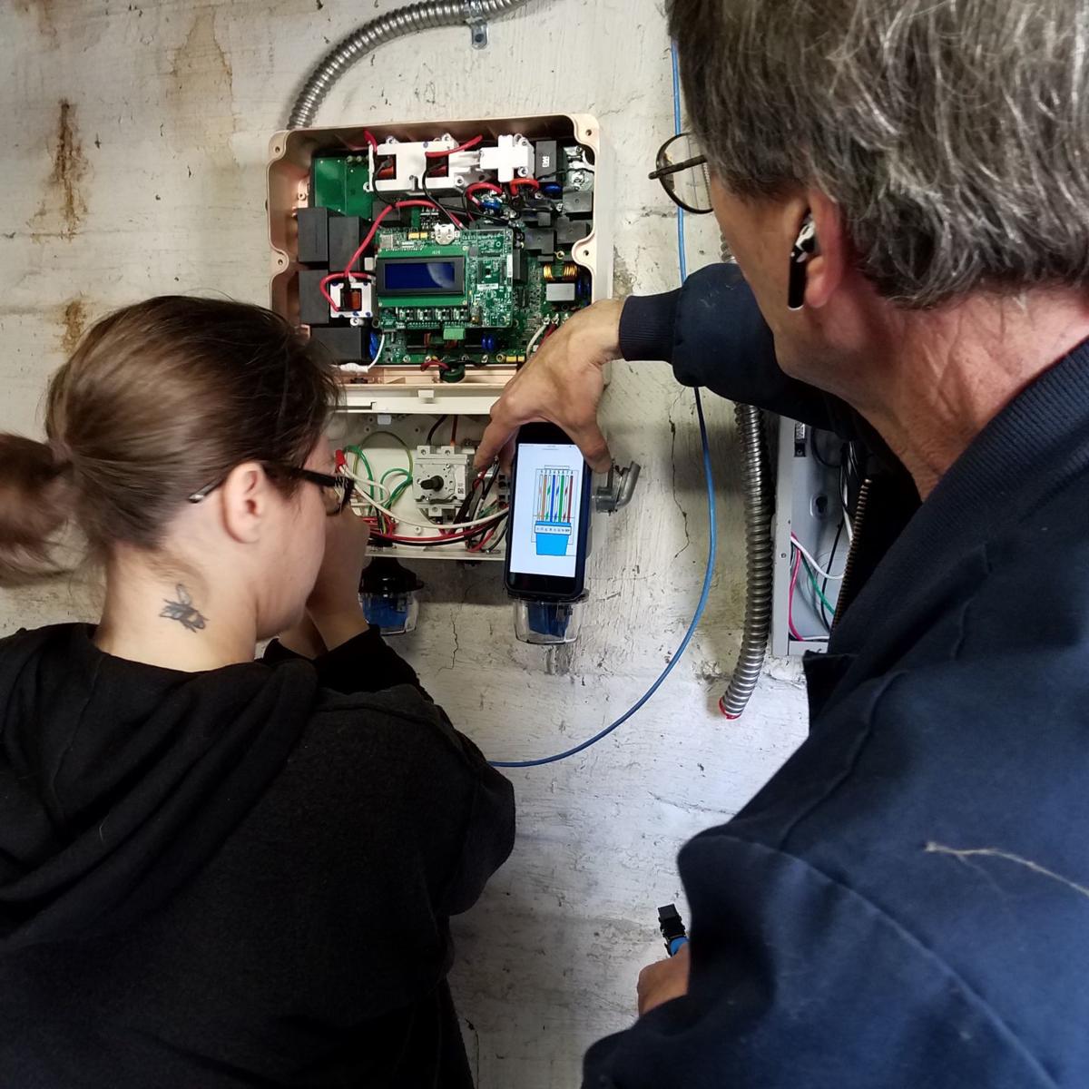 Woodie Bessler, right, a member of Solar Indiana Renewable Energy Network, teaches a volunteer how to wire an inverter that is part of a solar installation. (Anne Hedin / Courtesy photo)