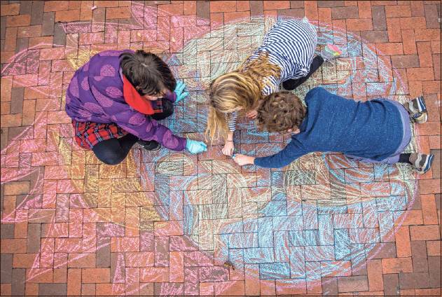 Maria Colvard, left, Tressa Martinie Eiler, middle, and Paul Martinie Elier work on coloring in a flaming Earth chalk drawing they did Friday. Staff photo by Rich Janzaruk