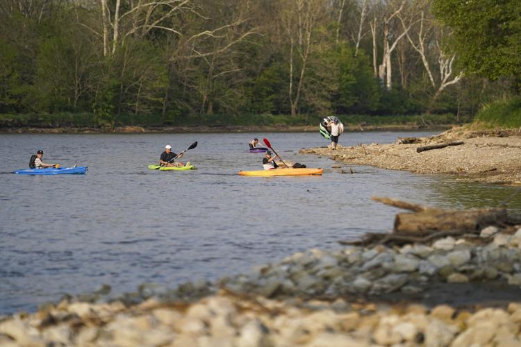Kayakers approach a bank along the Eel River as people with inner tubes walk behind them near Riverside Park in Logansport on Tuesday, May10, 2022. Staff photo by Jonah Hinebaugh