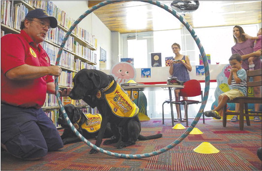Retired firefighter and paramedic Jeff Owens and Kalli, a 7-year-old black labrador retriever, demonstrate how to check the temperature of doorknobs to see if fire may be outside a room during the Fire Safety with Kasey program at the Galveston Public Library in Galveston on Thursday, July 21, 2022. Photo by Jonah Hinebaugh | Pharos-Tribune