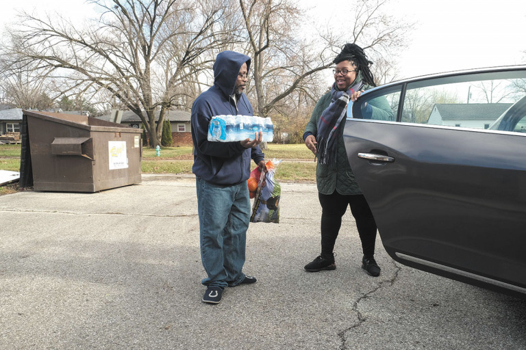 Eskenazi Health community health worker Simone Turner delivers food to Thomas Clark. Eskenazi hopes its planned Beyond Barries initiative will make deeper inroads into health equity by increasing access to health care, mental-health care, nutritious foods and other resources. (IBJ photo/Eric Learned)