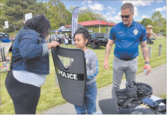 Alexis Harris, left, helps Phillip Watkins try out a shield as Mike Anderson, assistant chief of community policing for the Anderson Police Department, watches Saturday during APD’s first block party of the year, at Walnut Street Park. Andy Knight | The Herald Bulletin
