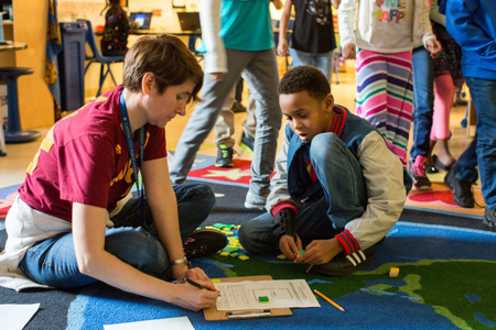 A teacher reviews a student’s completed work in a third-grade classroom as students rotate to new math stations. (Allison Shelley/The Verbatim Agency for EDUimages)